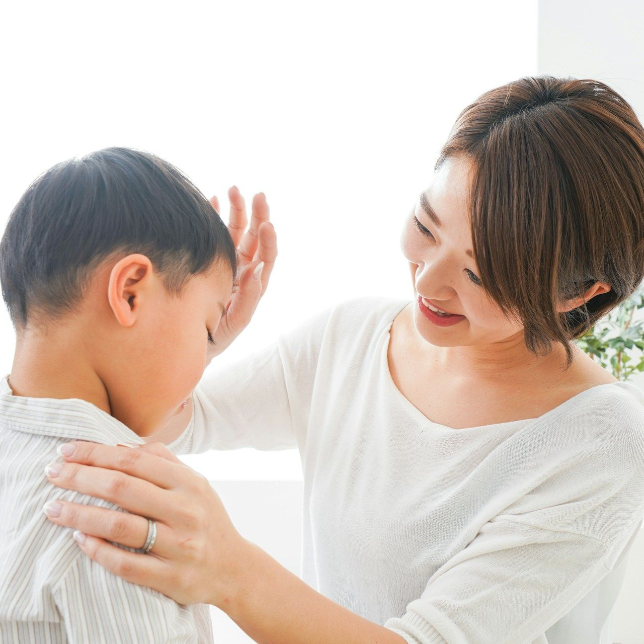 Woman comforting child, hand on head, smiling. Indoor setting, soft light.