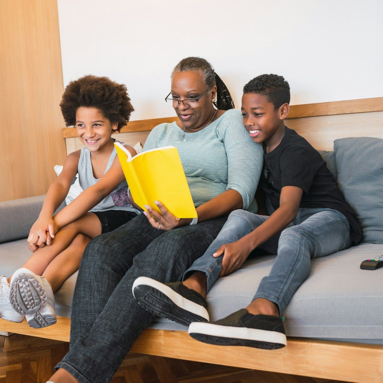 Woman reads aloud from a yellow book to two children on a couch.
