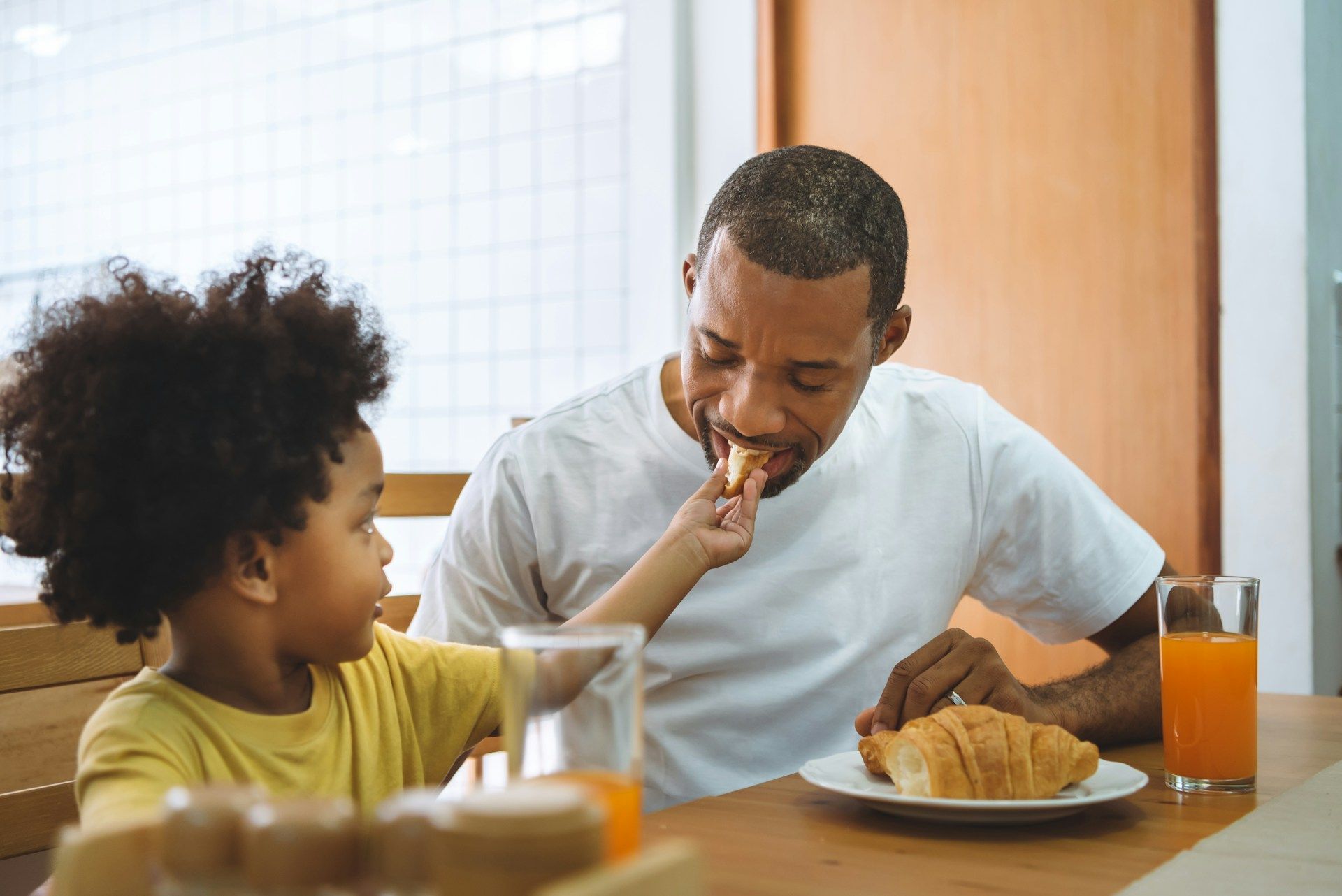 Child feeding bread to adult at breakfast table.