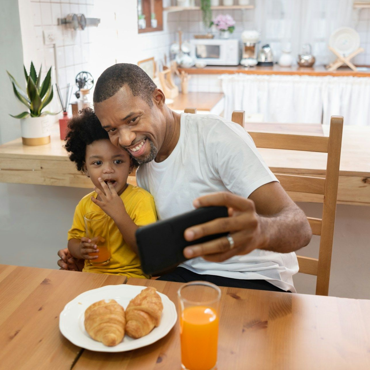 Man and child taking a selfie in a kitchen with breakfast.