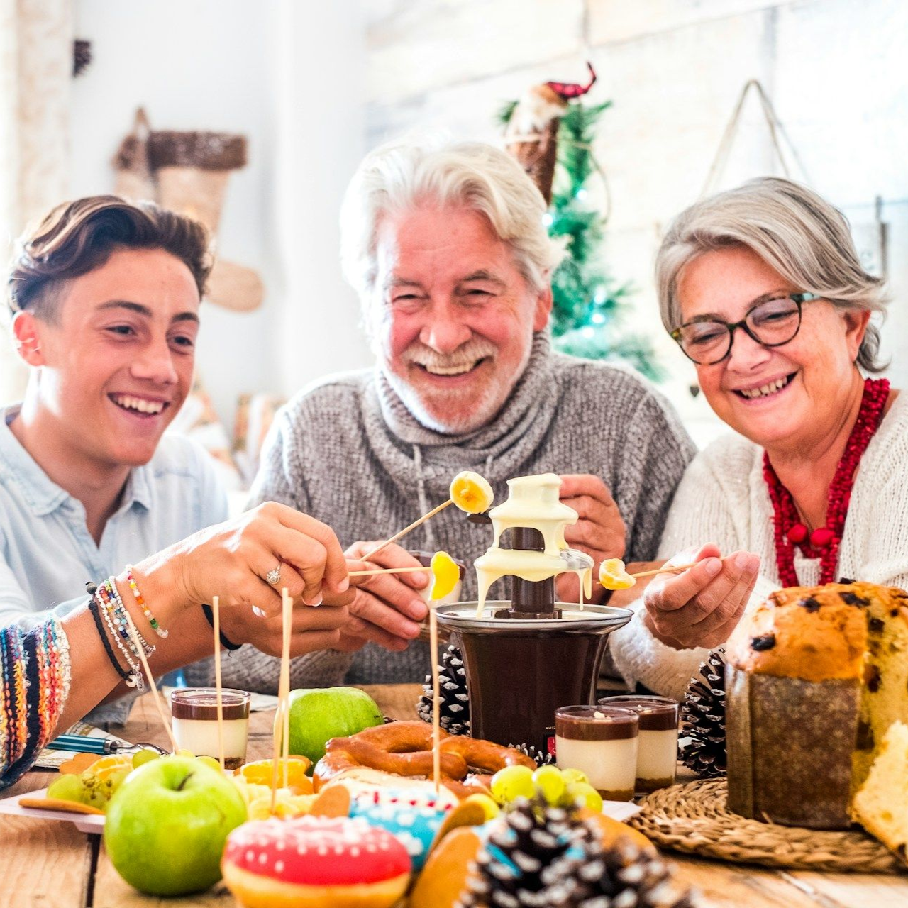 Family smiling, enjoying chocolate fountain and treats at table.