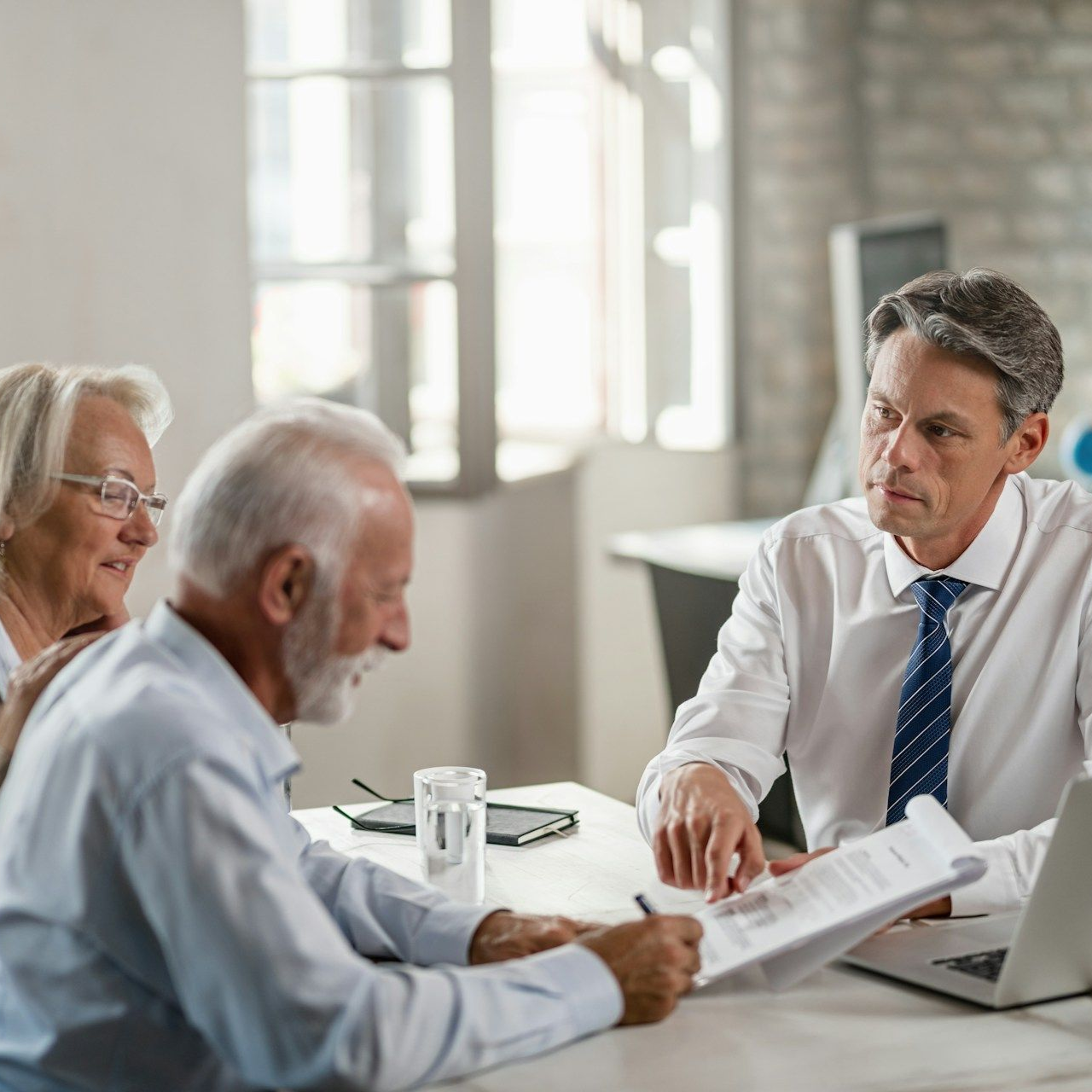 Senior couple signing a document at a desk with a financial advisor.