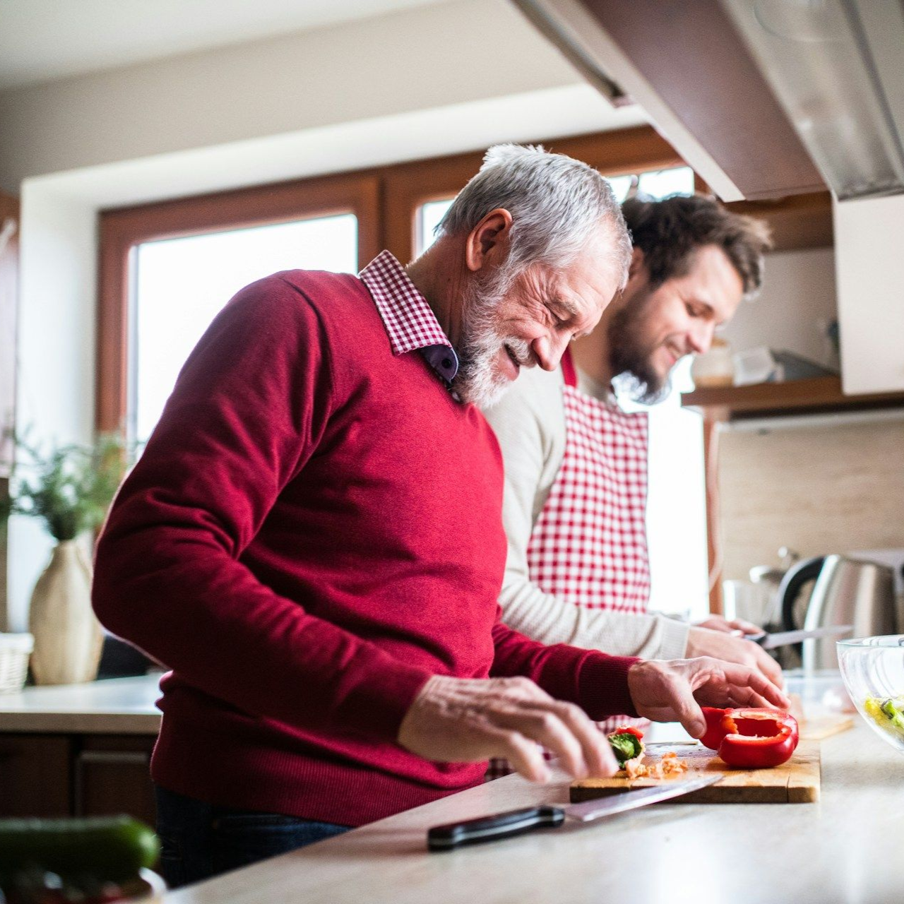 Man with gray hair and younger person preparing food in a kitchen.
