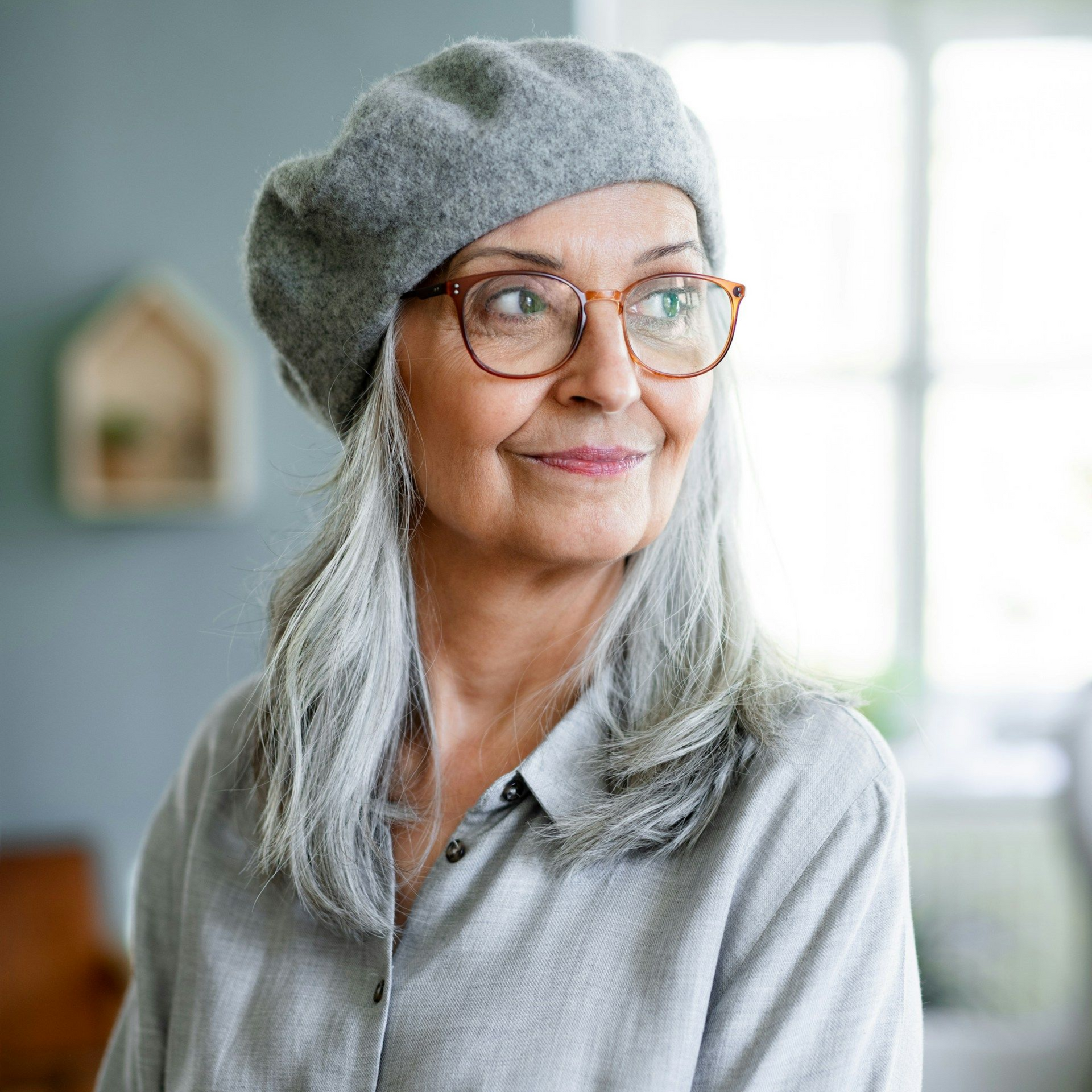 Woman with gray hair wearing glasses and a gray beret, smiling and looking to the side.
