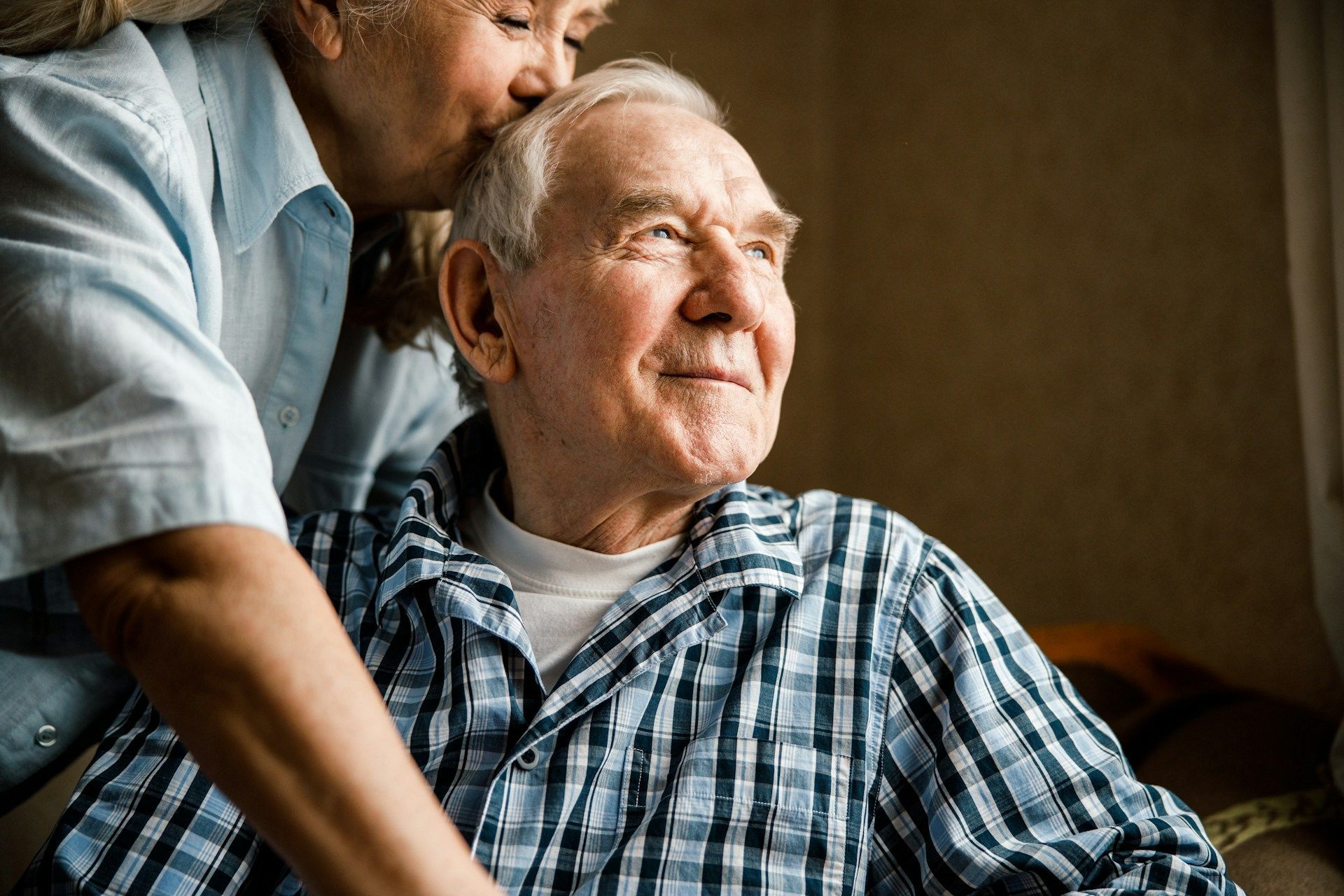 Woman kissing a smiling older man's forehead; indoor setting.