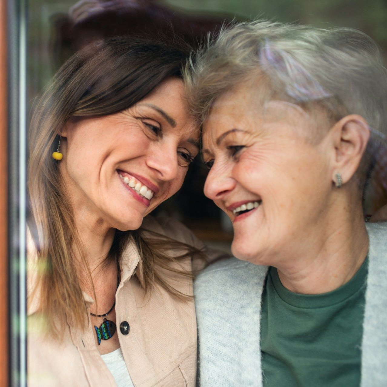 Two smiling people, leaning heads together. One has shoulder-length hair, the other has short hair.