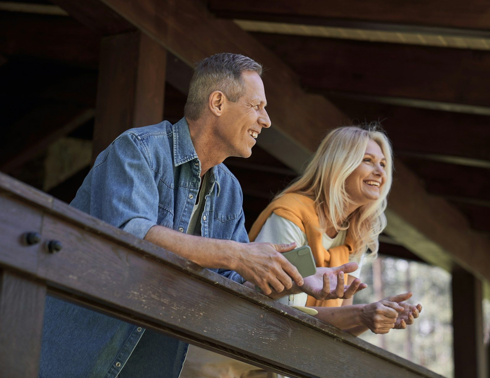 Smiling couple on a wooden porch, looking away, enjoying the view.