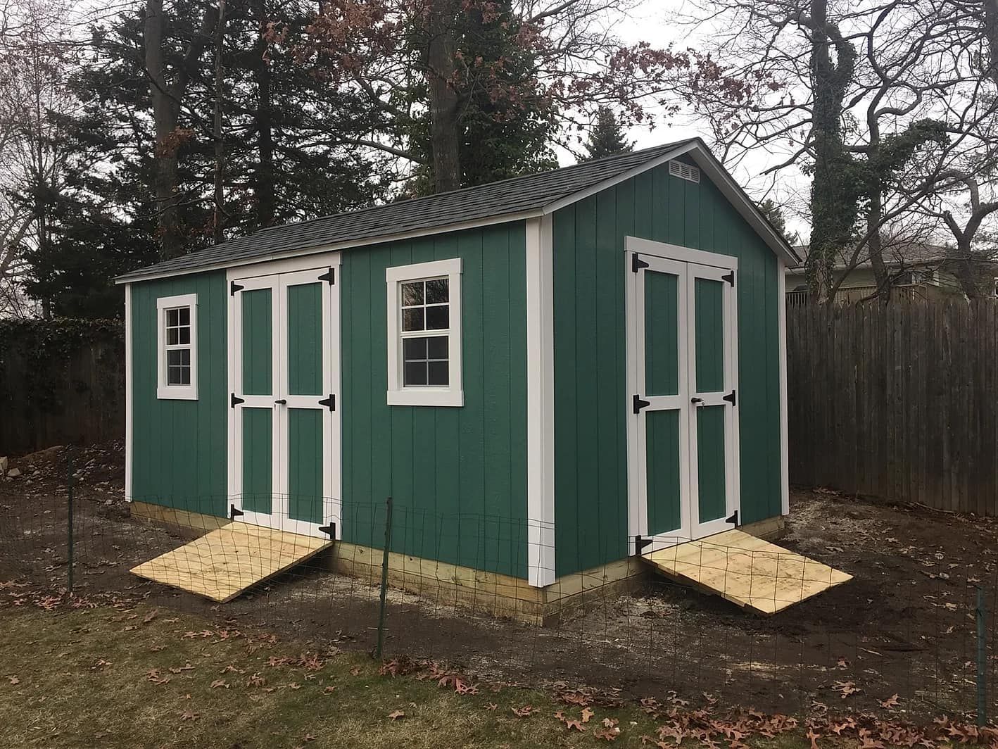 Green shed with white trim, two doors, and two ramps outdoors.