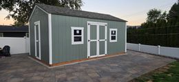 Green shed with white trim and doors on a paved patio.