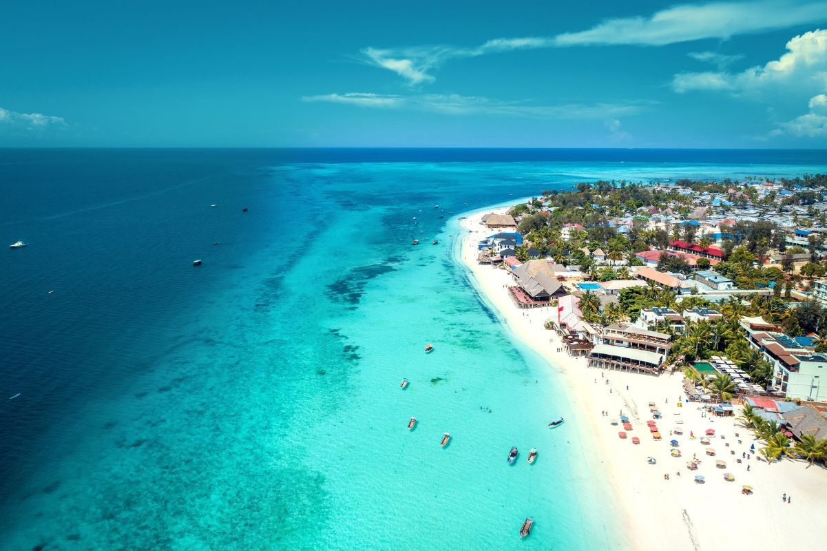 An aerial view of a tropical beach with turquoise water and a city in the background.
