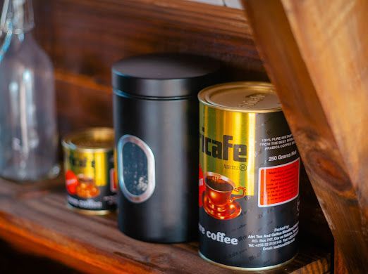 Three cans of coffee are sitting on a wooden shelf.