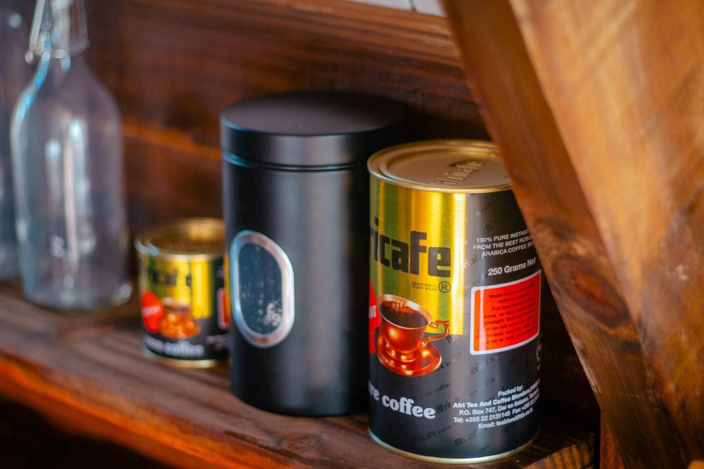 Three cans of coffee are sitting on a wooden shelf.