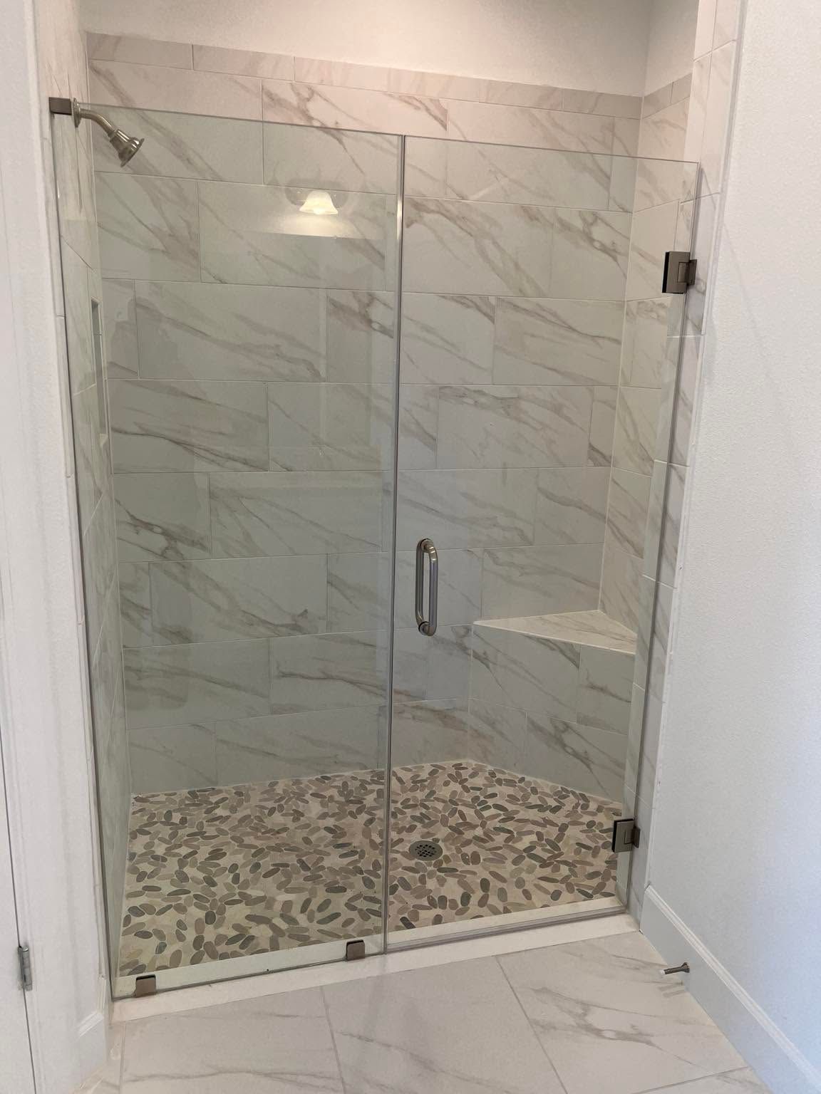 Glass shower enclosure with marble-look tile walls and pebble-pattern shower floor