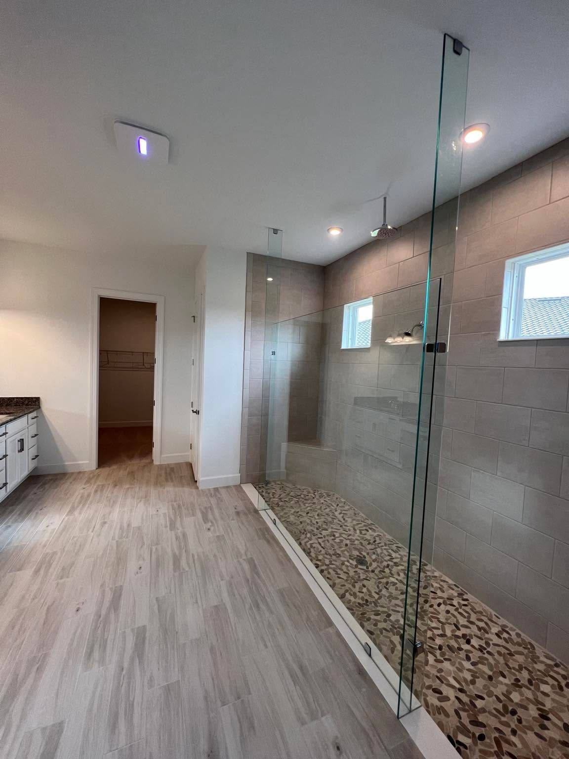 Modern bathroom with glass shower, pebble floor, and light wood-look tile flooring