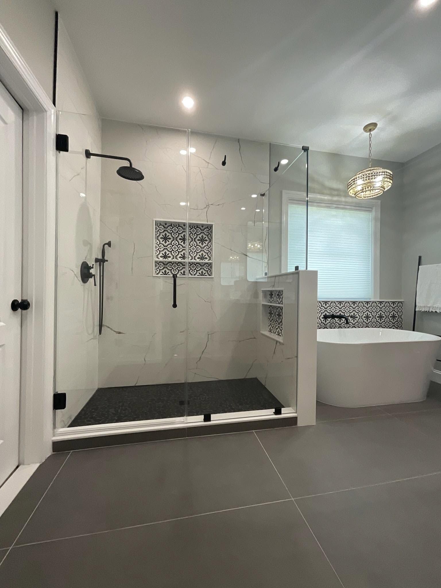 Modern bathroom with glass shower, black-and-white tile, and freestanding tub near a window.