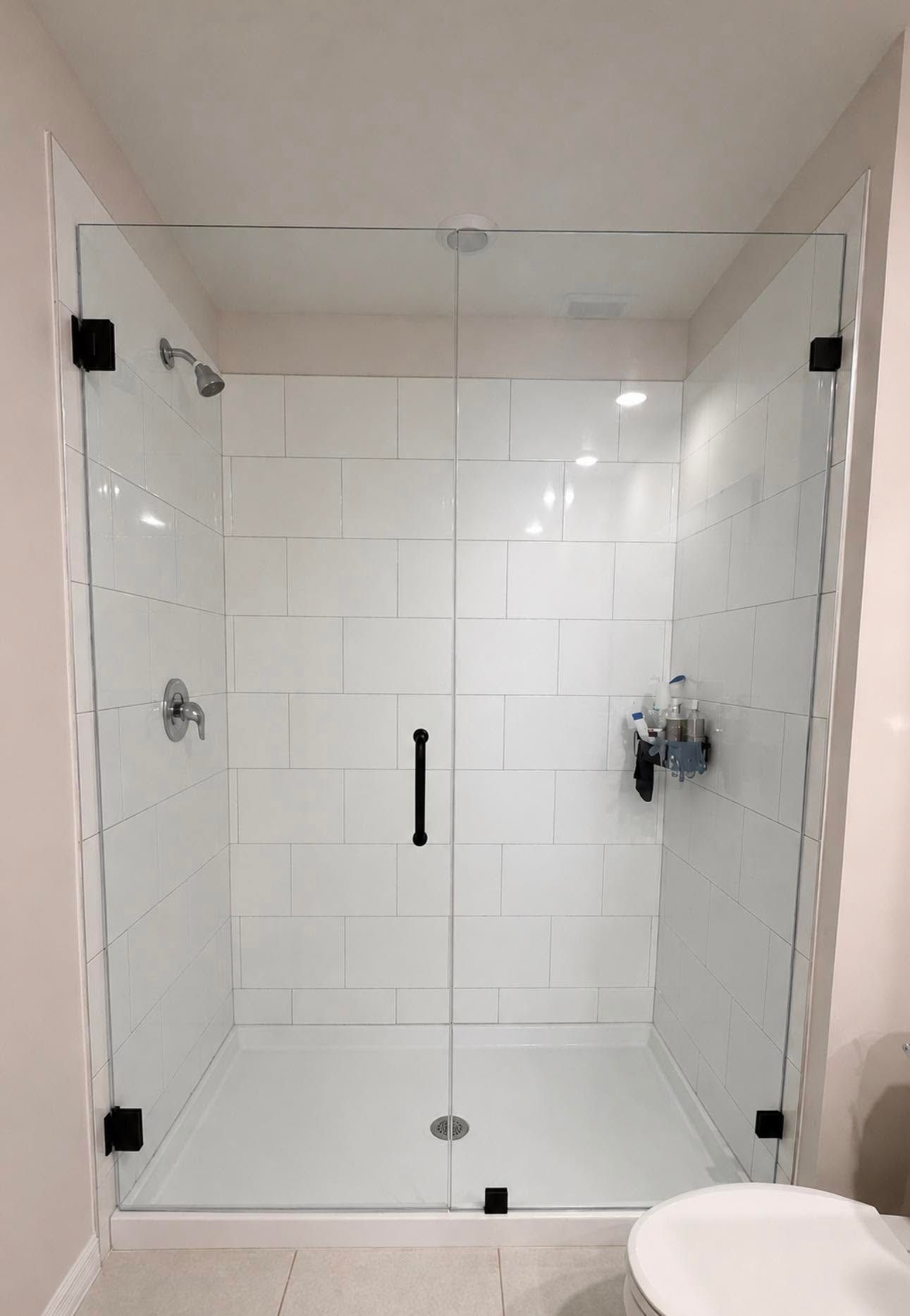Modern white-tiled shower with glass doors and chrome fixtures in a bathroom.