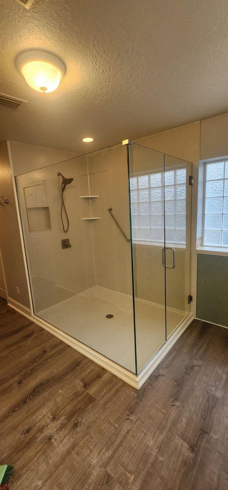 Walk-in shower with glass enclosure, white tile walls, and wood-look bathroom flooring
