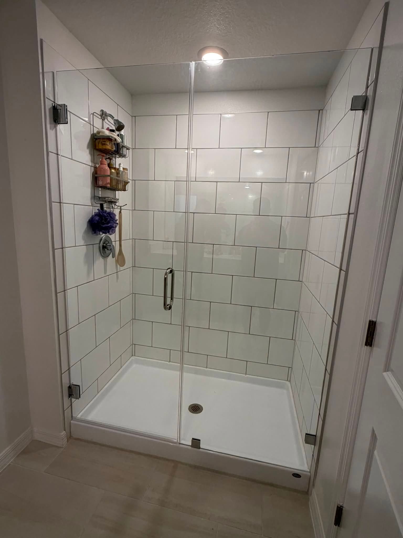 Glass shower stall with white tiled walls, built-in corner shelves, and tiled bathroom flooring.