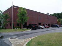 Brick building with parked cars in front, green lawn and trees.