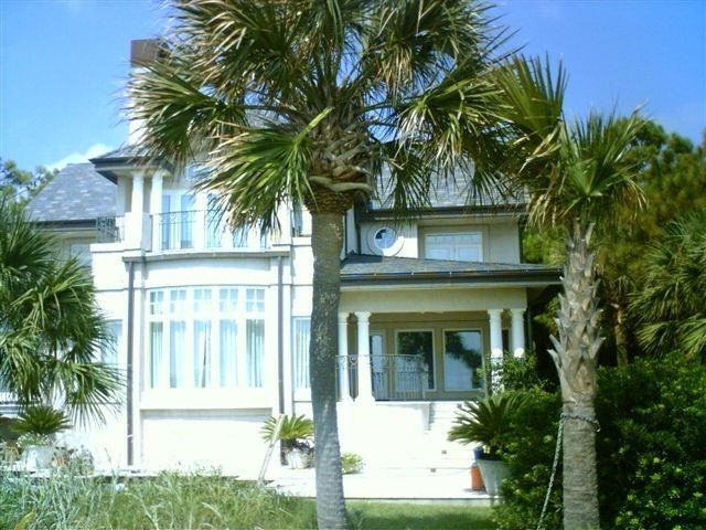 Two-story white house with palm trees in front, set against a blue sky.