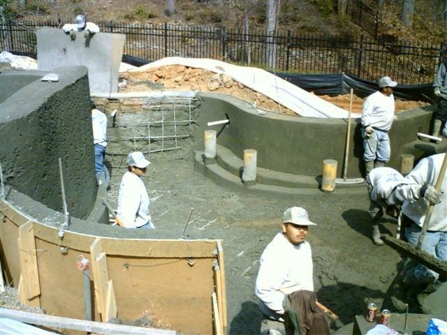 Construction workers applying concrete to a pool, using tools, outdoors.