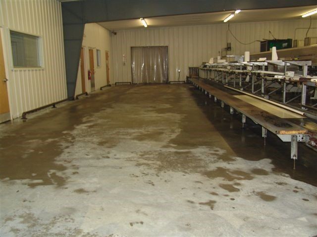Flooded industrial room with conveyor belt. Gray floor, white walls, and clear plastic door.