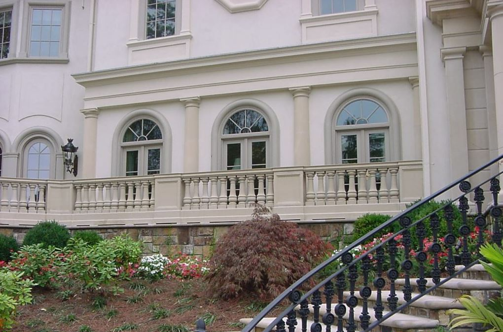 Beige mansion facade with arched windows, balcony, and black wrought iron staircase.