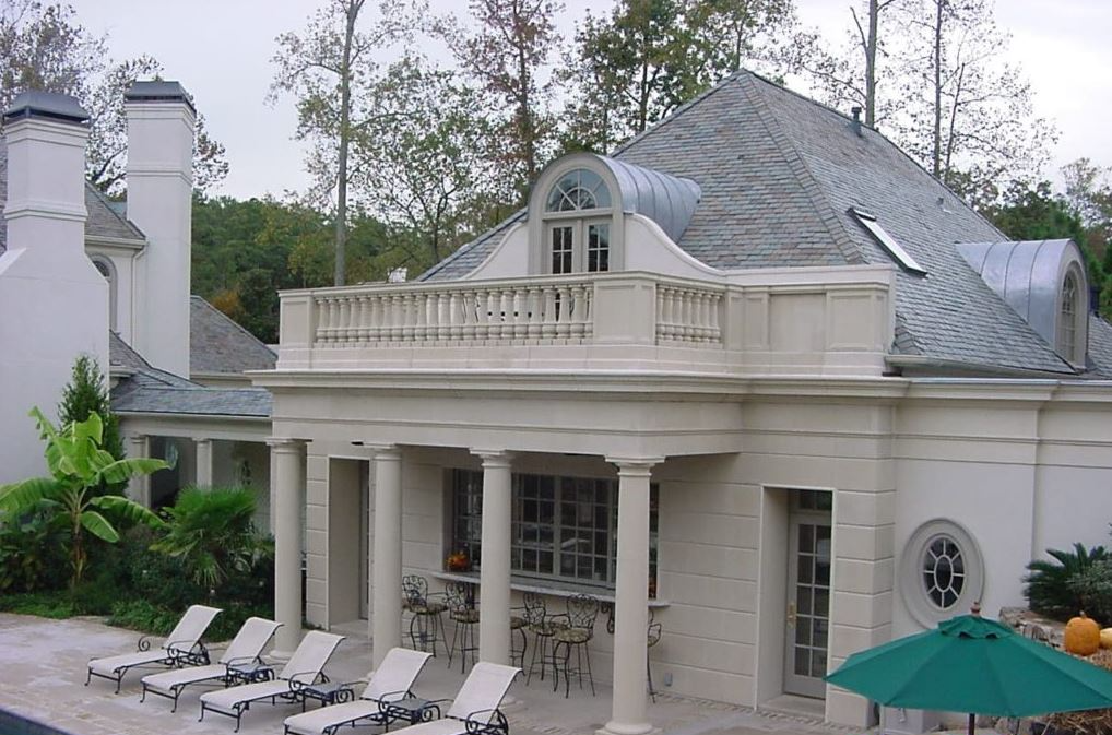 Luxury home with a pool, columns, and a balcony. Gray roof and light-colored exterior.