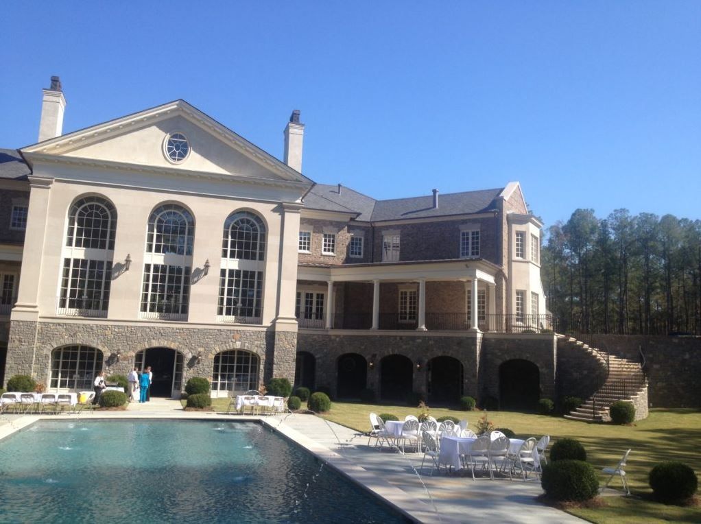 Luxurious mansion with a pool and patio; sunny outdoor setting.