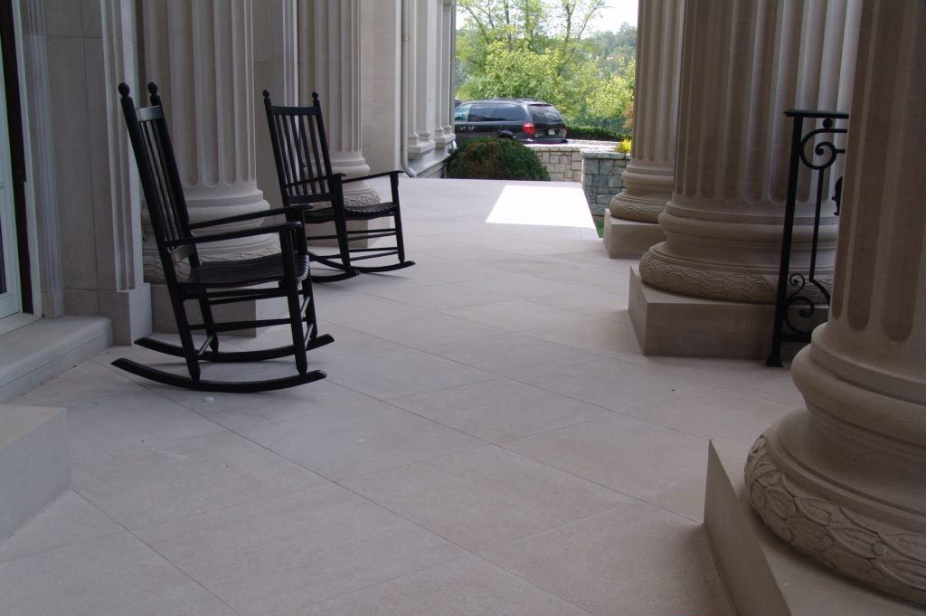 Two black rocking chairs sit on a white porch, framed by large stone columns.