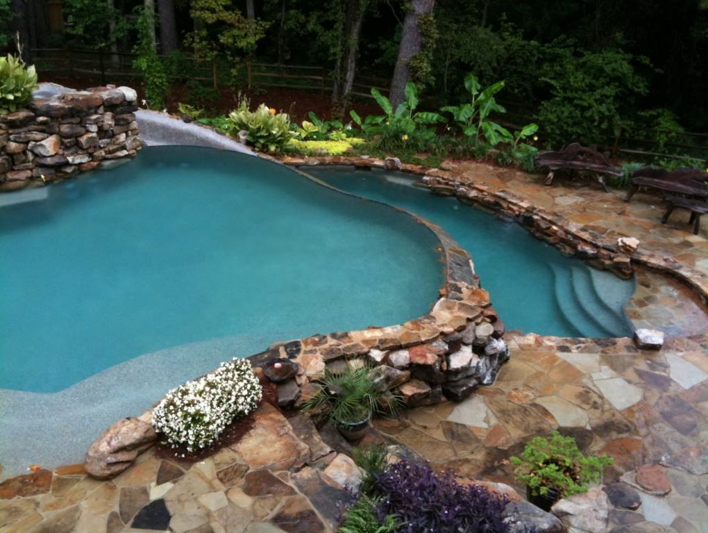 A pool with stone edging and steps surrounded by landscaping.