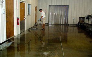 A man using a floor cleaning machine in a flooded warehouse.