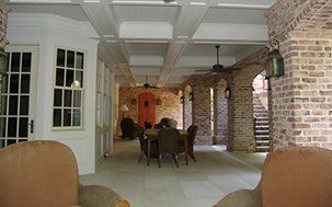 Covered patio with brick columns and ceiling beams, outdoor dining set, and stairs.