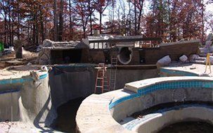 Pool under construction with surrounding building in a wooded area.