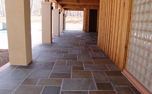 Covered porch with flagstone floor, wood siding, and beige pillars.