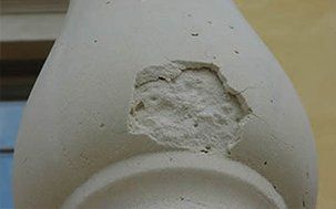 Close-up of a damaged, light-colored concrete baluster with a large chunk missing, revealing the rough interior.