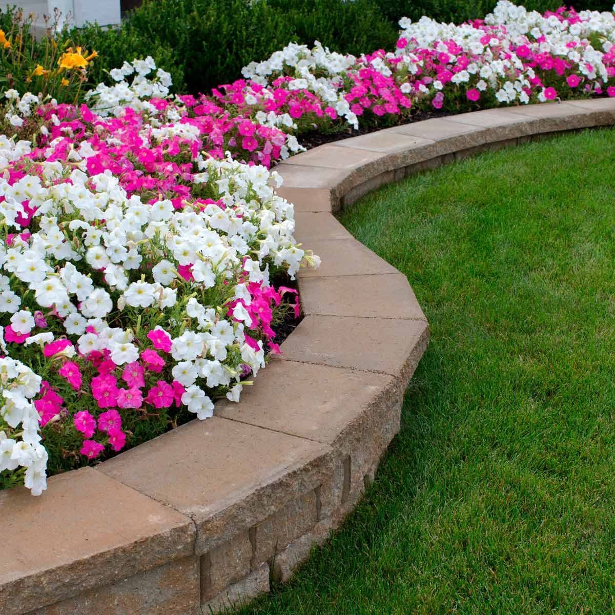 Curved stone garden border with pink and white flowers beside a green lawn