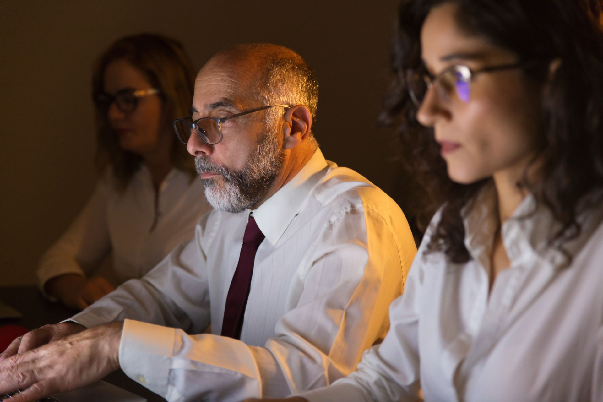 Tres personas con camisas blancas miraban fijamente una computadora en un entorno poco iluminado.