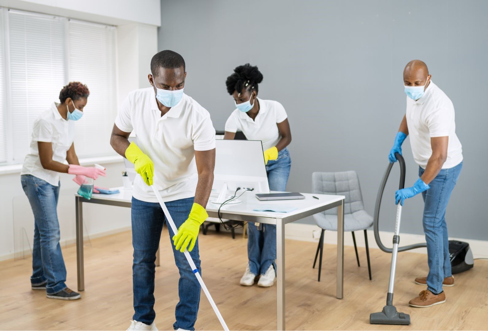 A group of people wearing masks and gloves are cleaning an office.