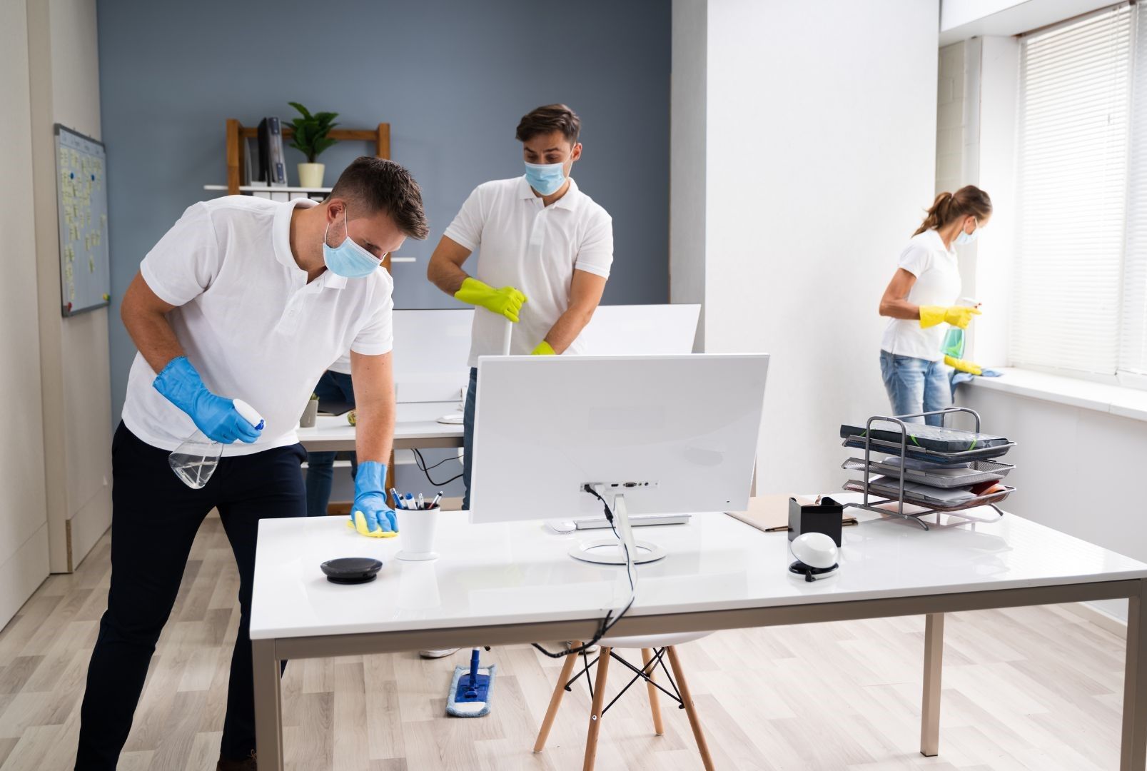 A group of people wearing masks and gloves are cleaning an office.
