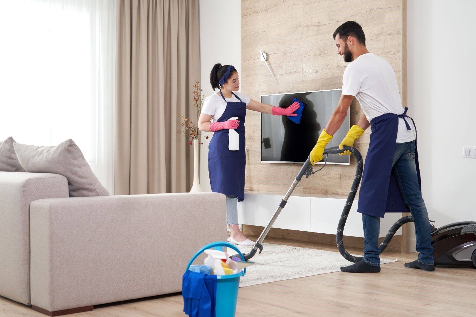 A man and a woman are cleaning a living room with a vacuum cleaner.
