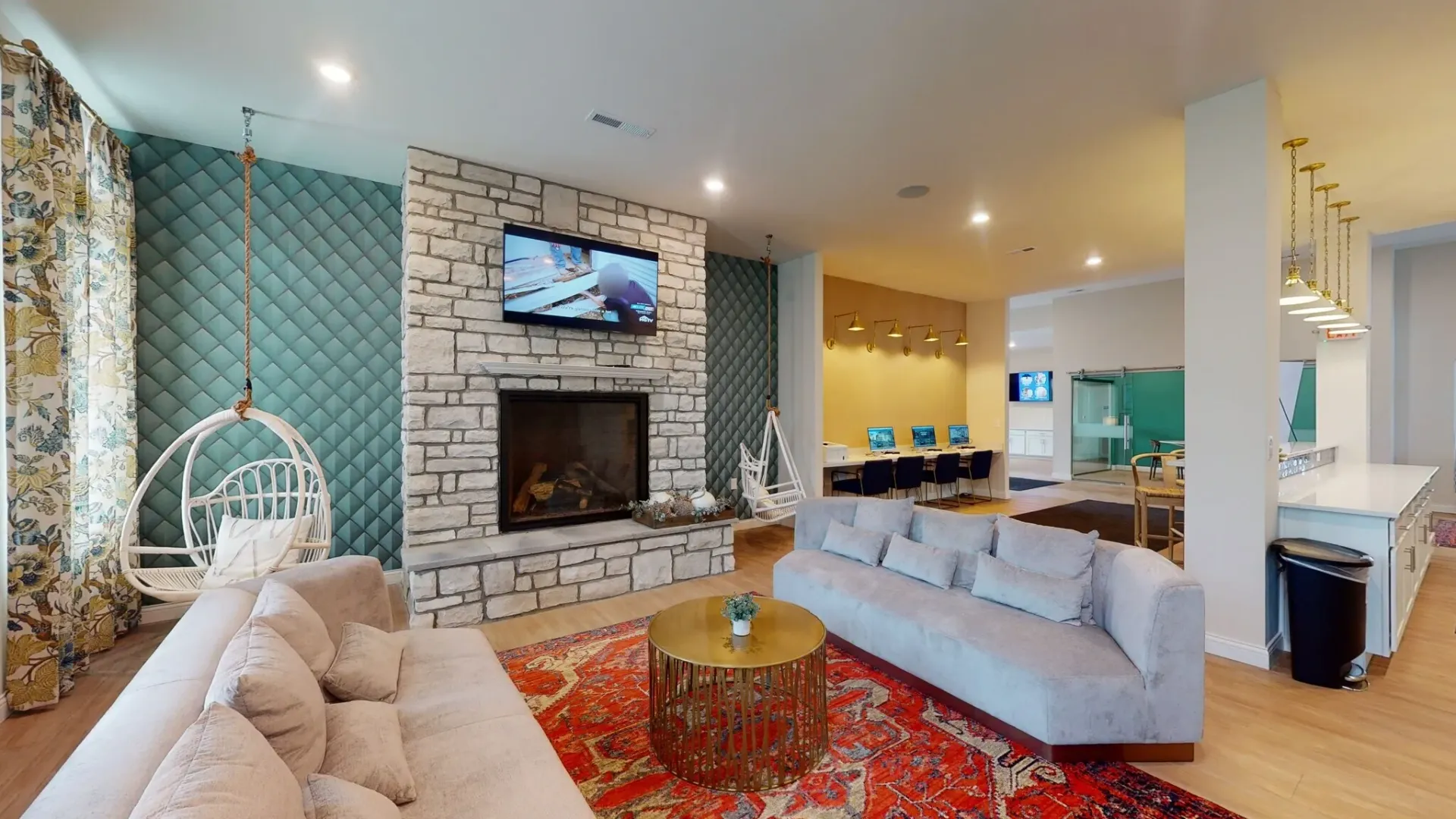 A modern lobby with a stone fireplace, hanging chair, gray sofas, gold coffee table, and an open computer area.