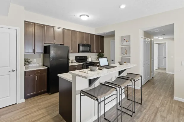A modern kitchen with dark brown cabinets, a black refrigerator, a granite countertop island, and three bar stools.