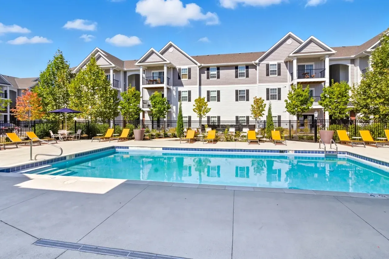 Outdoor swimming pool with lounge chairs and apartment buildings in the background.