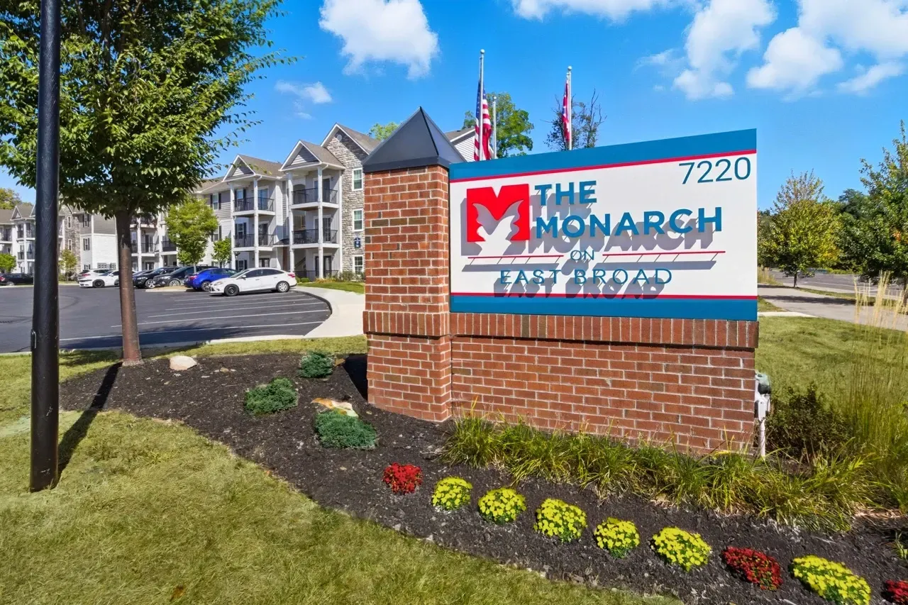 The Monarch on East Broad monument sign with apartment buildings and parking lot in the background.