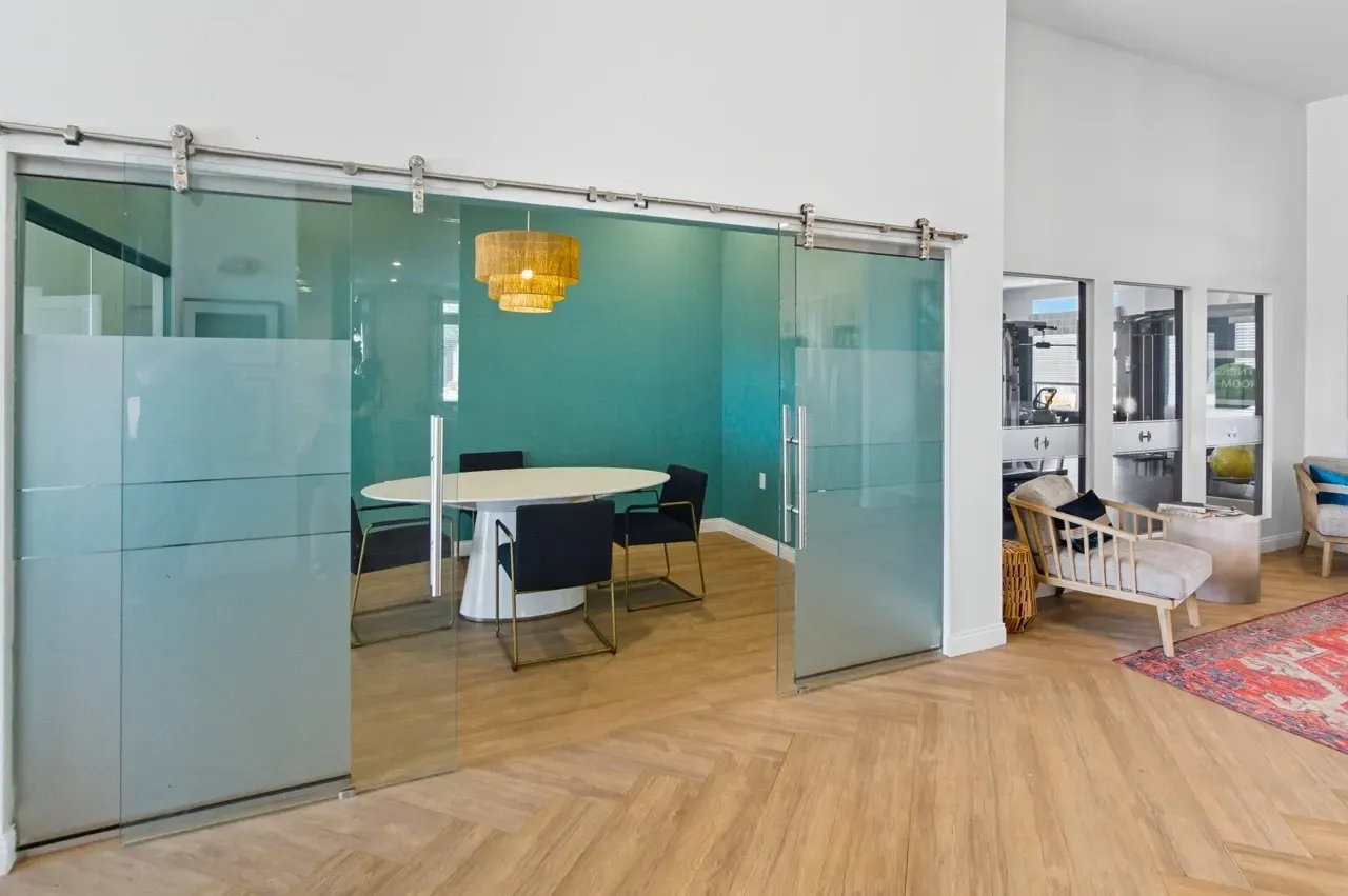 Modern meeting room with glass barn doors, a white oval table, and teal walls.
