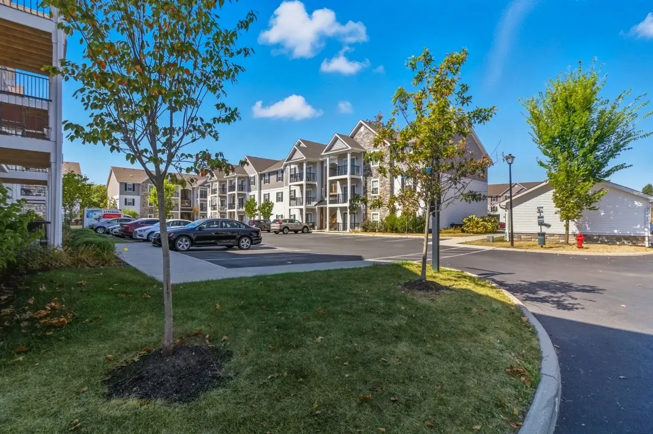 Apartment building exterior with parking lot and trees.