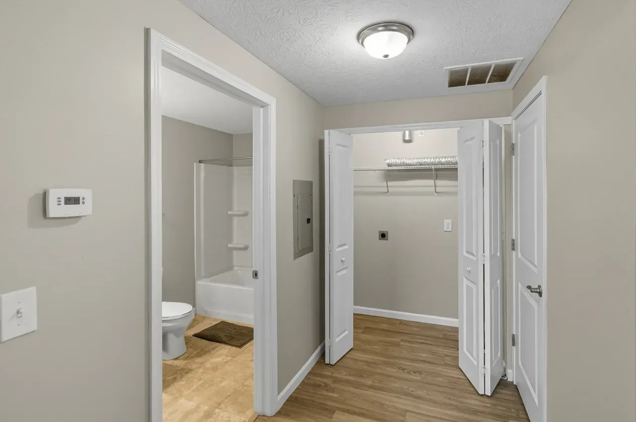 Hallway view of a bathroom with a toilet and tub, and a laundry closet with washer/dryer hookups.