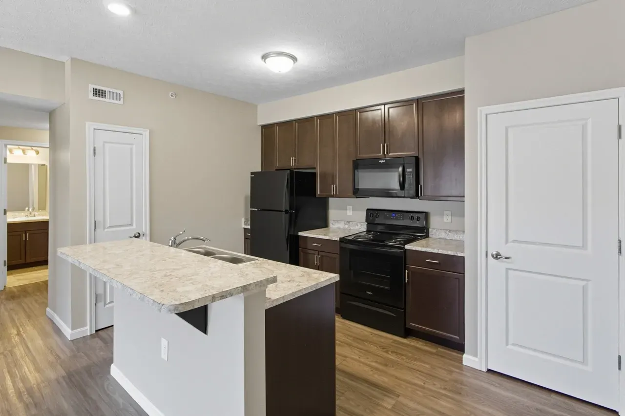 Modern kitchen with dark wood cabinets, a large island, and black appliances.