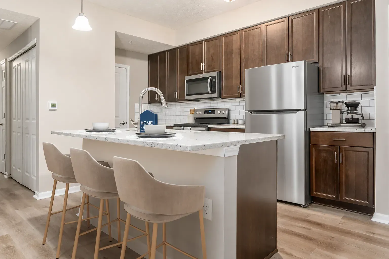 Modern kitchen with island, beige bar stools, stainless appliances, and wood cabinets